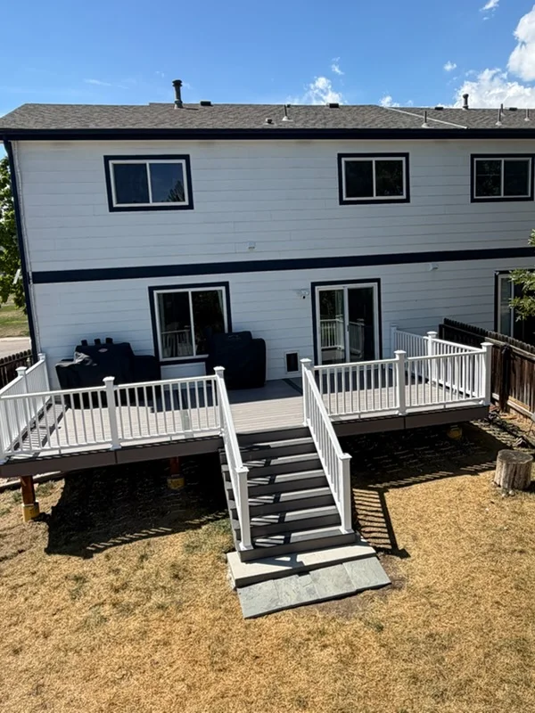 Two-level composite deck with white railings, black stairs, and gravel ground area