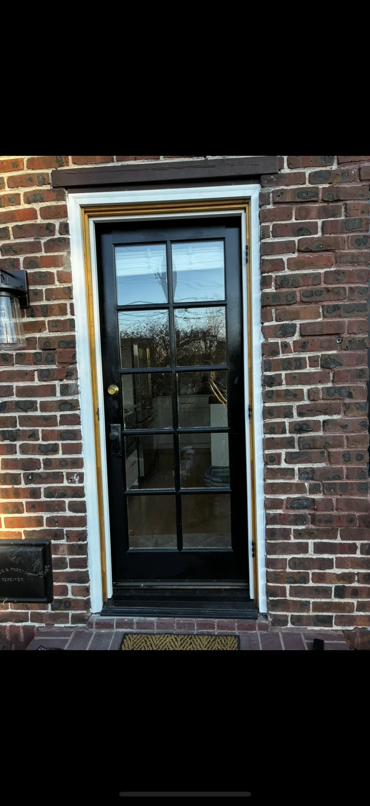Black French door with ten glass panes, white trim, brass hardware in brick wall