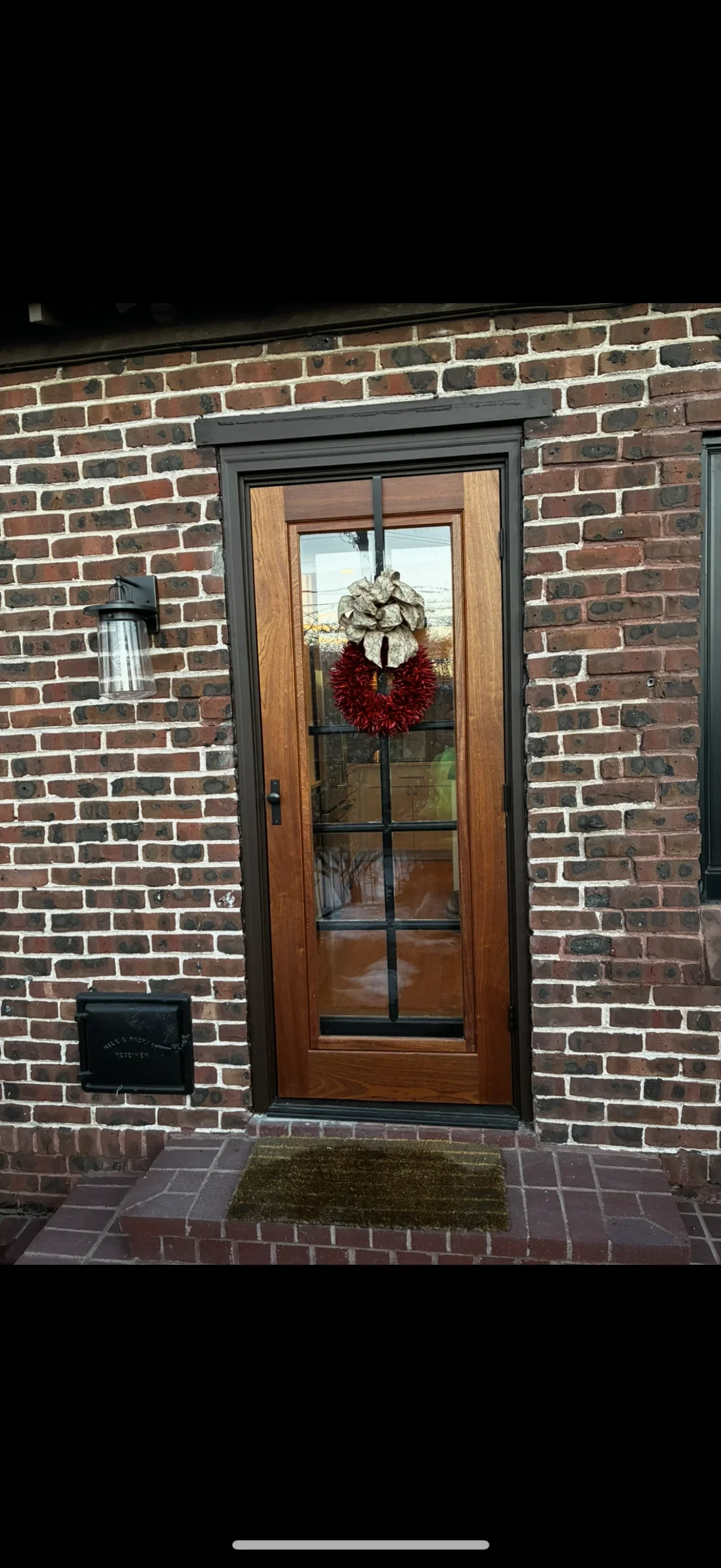 Wood entry door with glass panes set in black frame against red brick wall