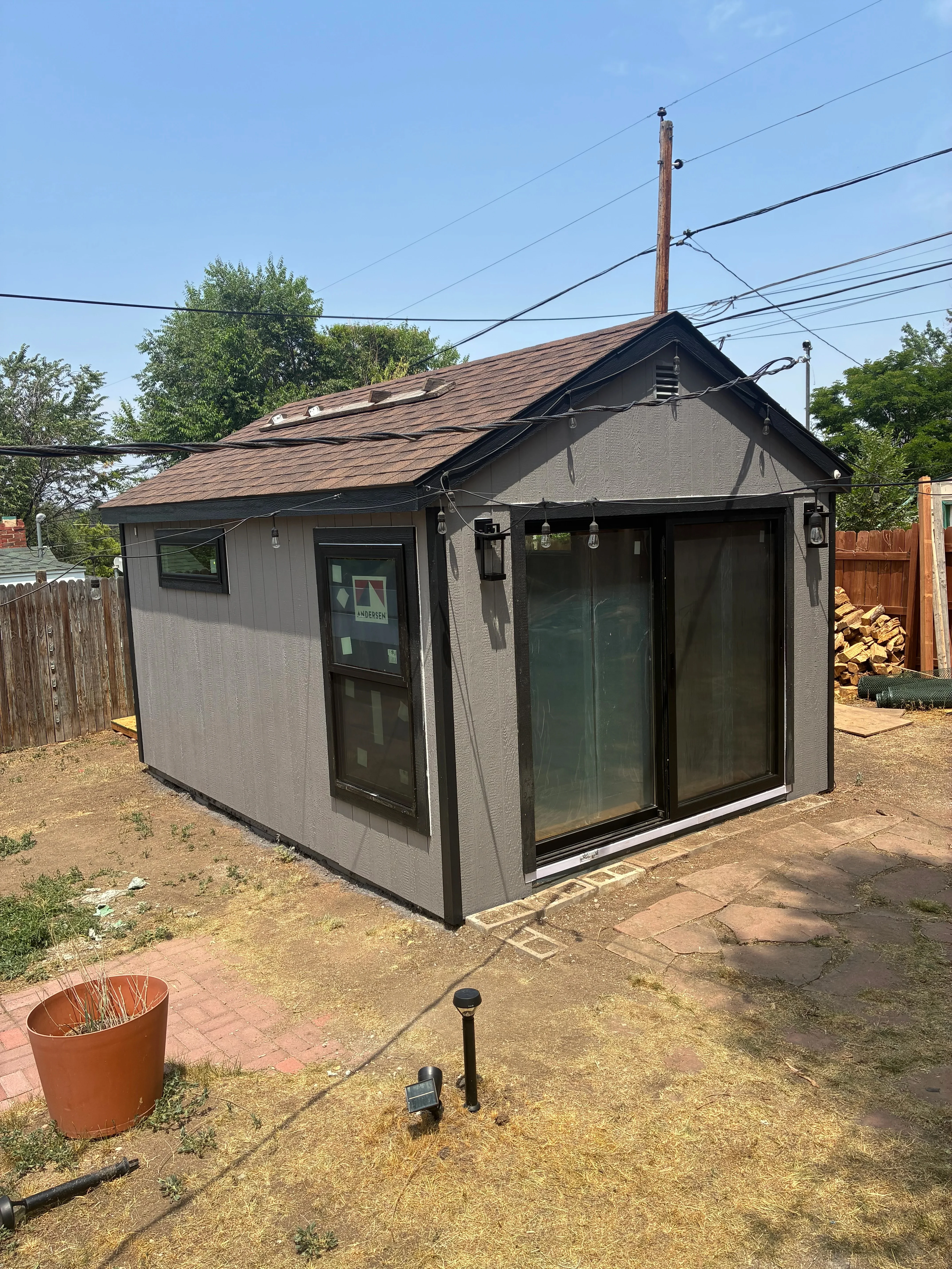 Gray composite siding shed with black trim, pitched roof, and large sliding glass doors
