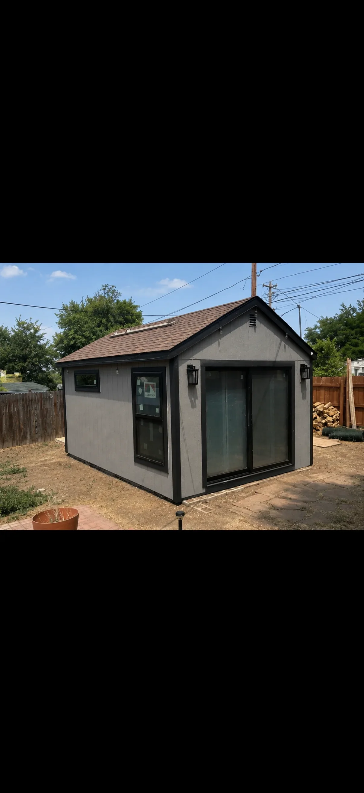 Gray composite siding shed with black trim, peaked roof, and glass sliding doors