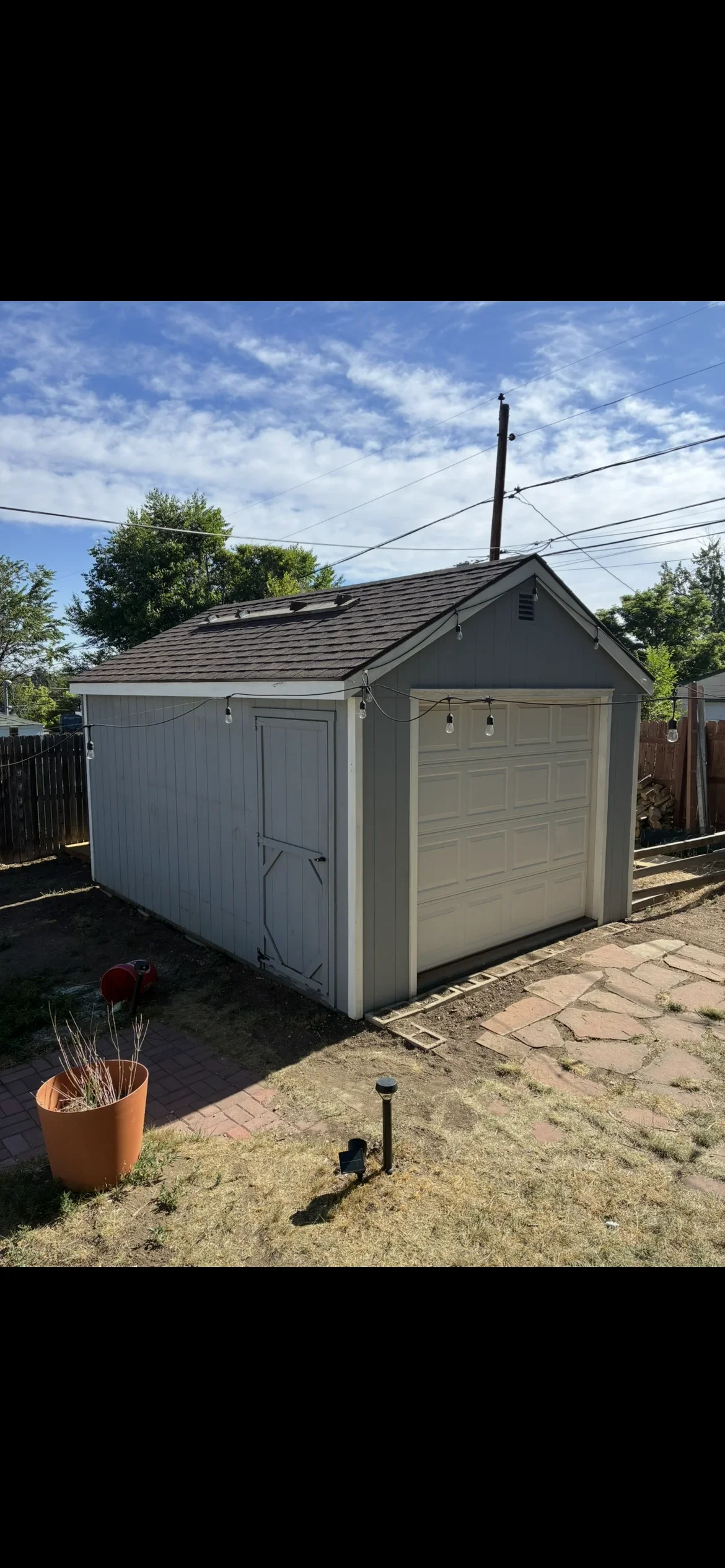 Two-bay storage shed with gray siding, garage door, hinged entry door, and asphalt shingle roof