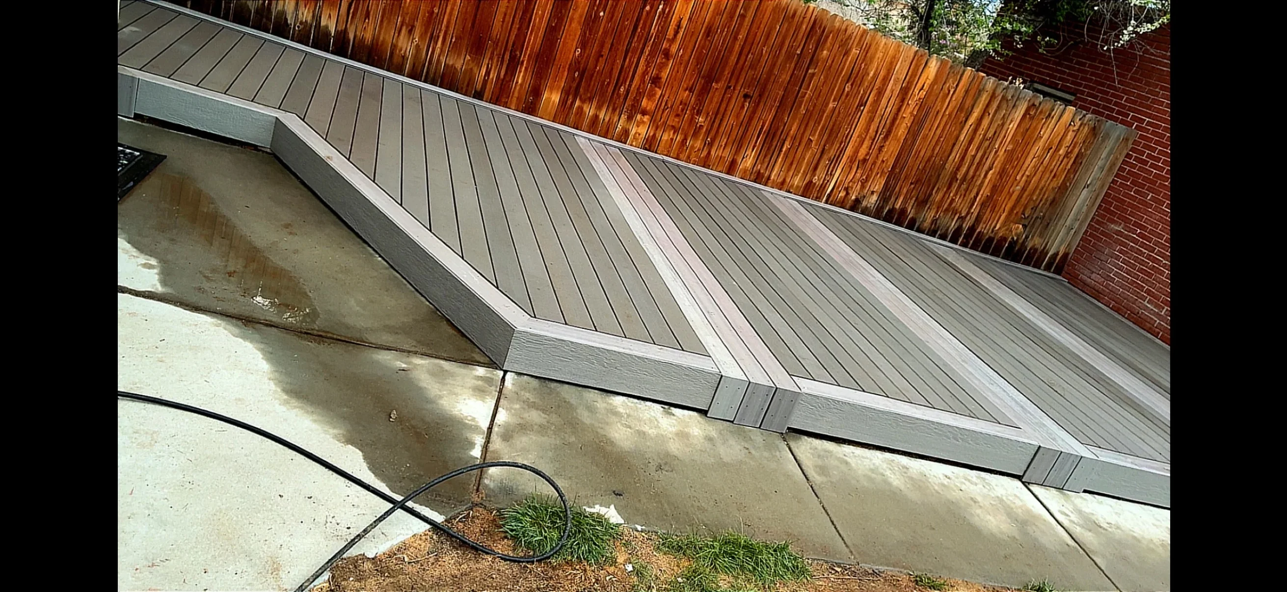 Gray composite deck with diagonal board pattern and metal fascia trim over concrete base